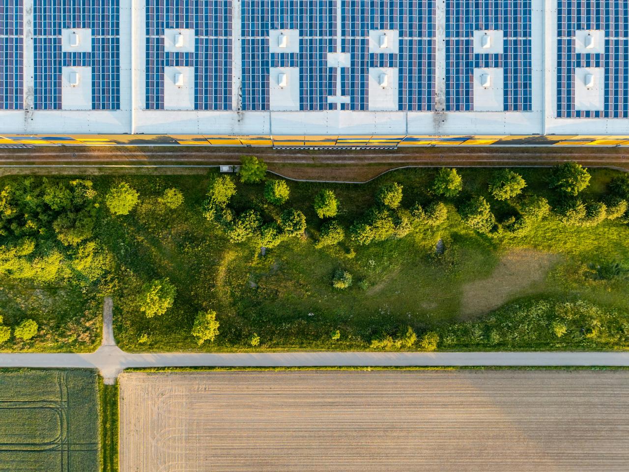Panel surya menghiasi sebuah bangunan, dengan ladang di bawahnya.